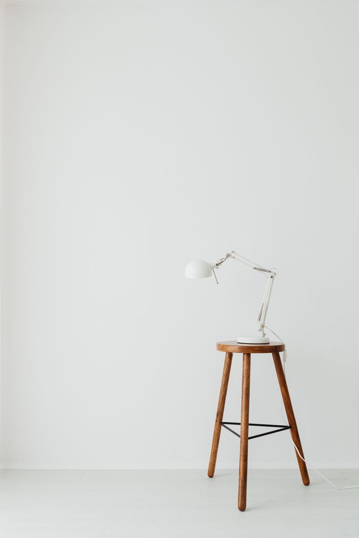 Simple and elegant minimalist setup featuring a desk lamp on a wooden stool against white walls.