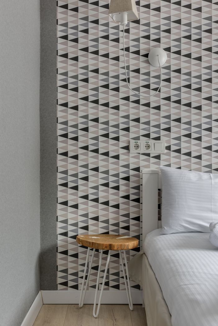 Modern bedroom corner featuring geometric wallpaper, a bed, and a wooden stool.